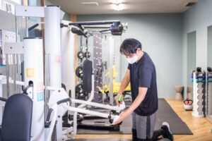 フィットネスジムのトレーニングマシンを清掃するスタッフ